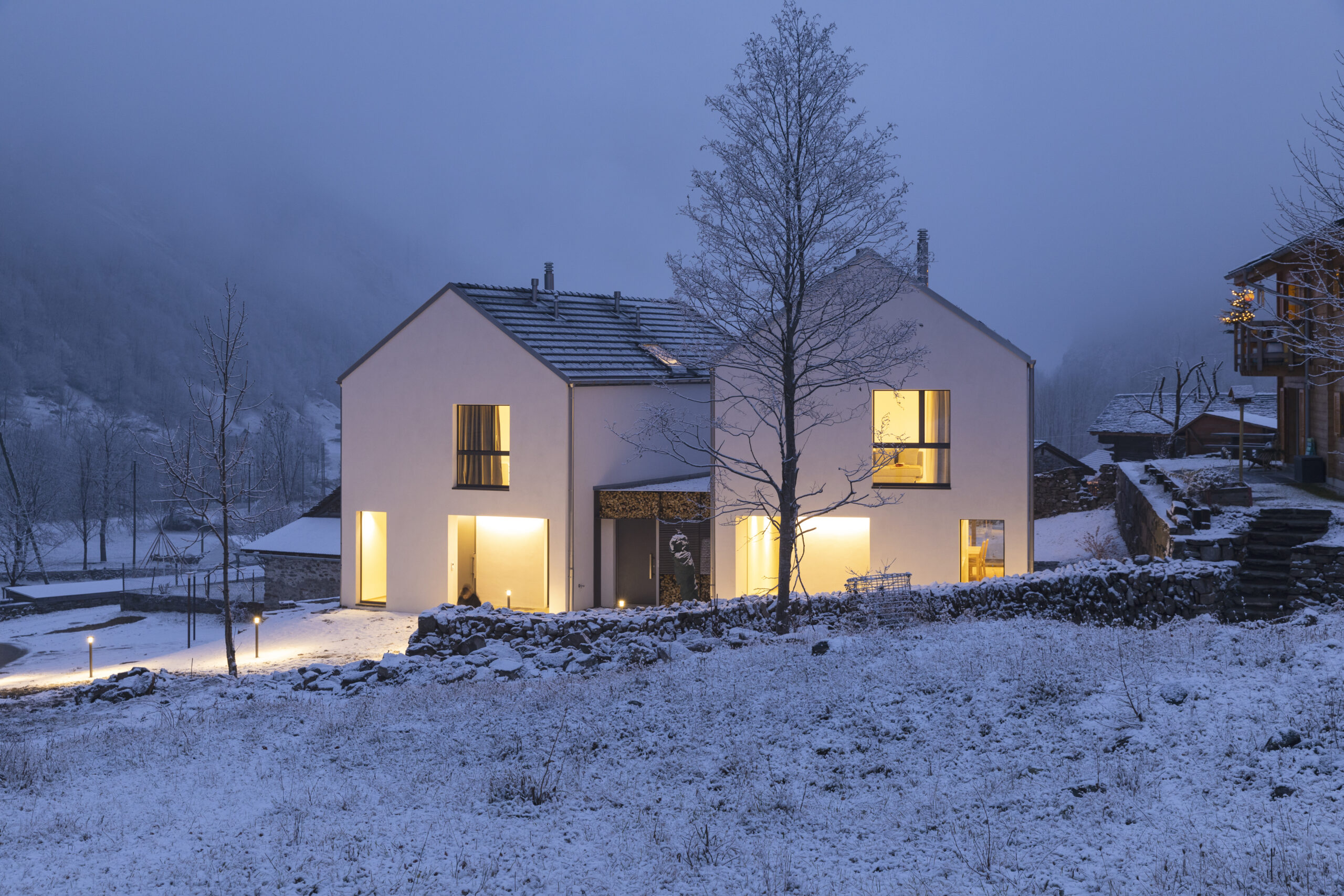 Modern white house with light windows surronded by mountain, snow and trees. Chirstmas mood Modern white house with light windows surronded by mountain, snow and trees. Chirstmas mood. Nobody inside.